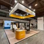 Exhibition stand featuring central demo area with digital screens and branded elements